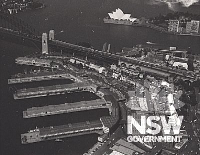 Aerial view of Walsh Bay Wharves showing wharves, shoresheds, bond stores and interconnecting bridges and relationship to Millers Point (below bridge approach).
