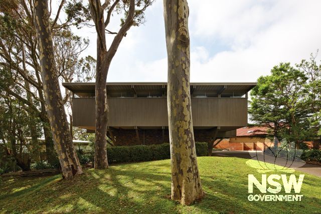 Photograph of façade of Lyons House to Port Hacking Road designed by Robin Boyd in 1967. Note sandstone fence, driveway and grass-covered hill providing bed for gum trees planted by Bruce Mackenzie.