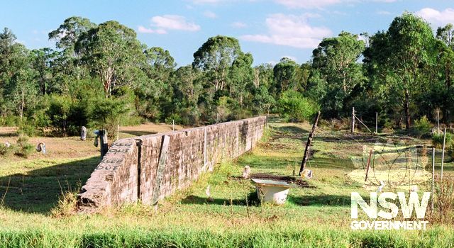 Remnant platform wall of Holmesville Railway Station (HV-24 and RT-09) located west of Margaret St, next to Killingworth Rd. Viewed from N, showing the platform side of the brick wall. Earth fill has been removed. (Doring Neg.308.14a)