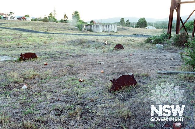 Looking S-W across the Colliery site to the coal box piers (centre) & soccer ground dressing shed (R-background). Half-buried iron discs in the foreground are anchor bases of the former backstays for the (part-removed) headframe (R). (Doring Neg.304.19)