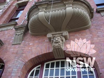 Decorative carved stone below oriel window & one of five sculpted heads decorating keystones over arches at street level